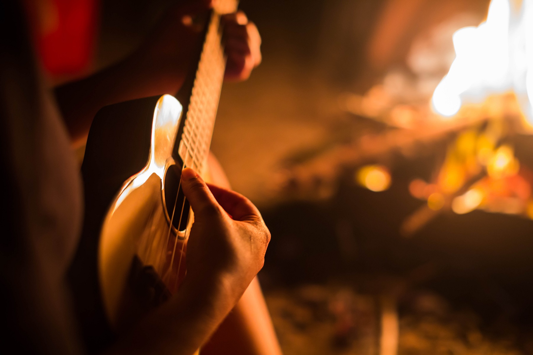 A female musician playing guitar outside, sitting next to a fire. Relaxation. Bonfire