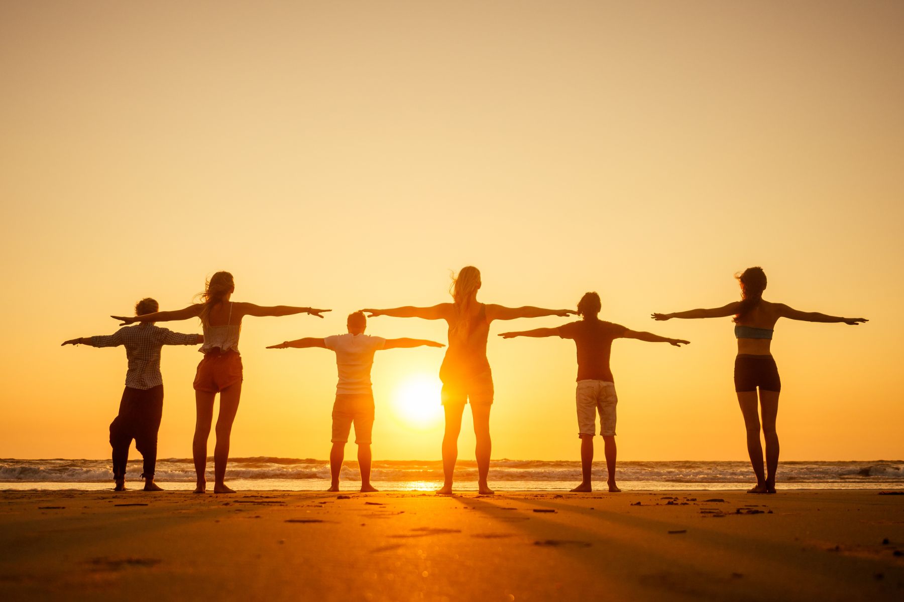 group of friends practicing yoga on the beach